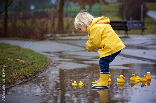 Obraz na plátně Beautiful funny blonde toddler boy with rubber ducks and colorful umbrella, jump