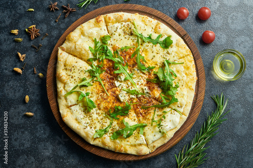 Homemade baked pizza with four types of cheese, white sauce, sesame and ruccola on a black background in a composition with ingredients.
