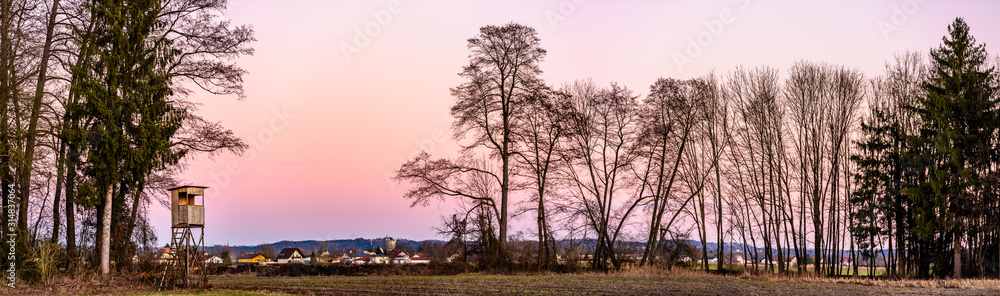 Obraz premium Panorama landscape with hunting tower after sunset in rural scenery against pink sky. Deer stand near Zettling Graz in Austria. Hunting concept