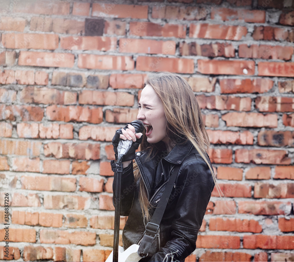 Beautiful young girl rocker with electric guitar. A rock musician girl in a leather jacket with a guitar sings. A rock band soloist plays the guitar and screams into the microphone.