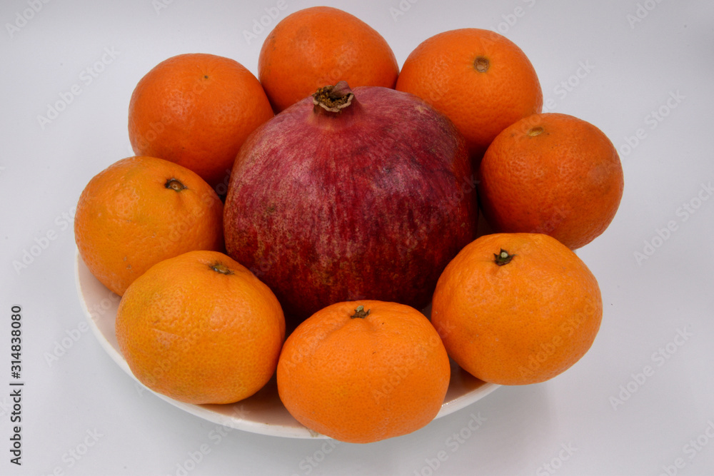Orange tangerines are placed in a circle on one plate, and in the center is a large, red pomegranate. Fruit on a plate. Orange tangerines are placed in a circle on one plate, and in the center is a large, red pomegranate. Fruit on a plate.