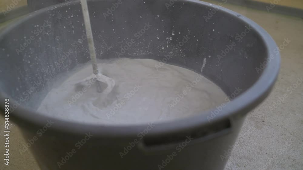 The mixer in the bucket mixes the mixture. The primer is mixed in a large bucket using a construction mixer. The mixer in the bucket mixes the mixture. The primer is mixed in a large bucket using a construction mixer.