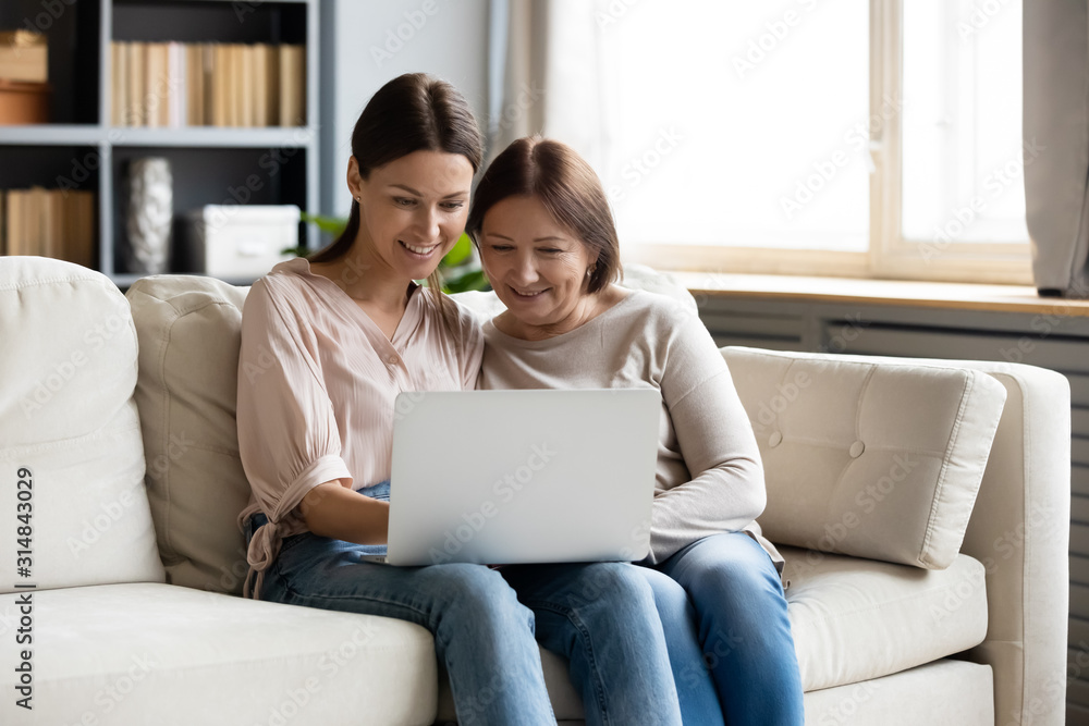 Smiling adult mom and daughter using laptop together Smiling adult mom and daughter using laptop together