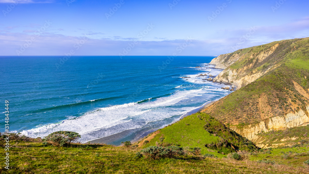 View of the Pacific Ocean coastline, with green grass covering cliffs and bluffs, on a sunny day, Point Reyes National Seashore, California
