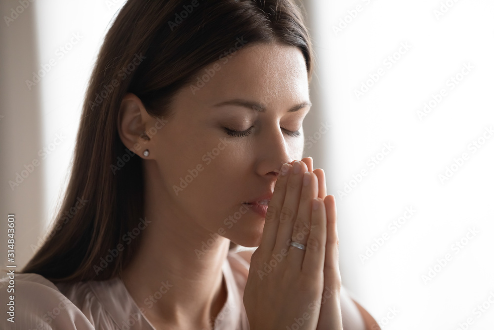 Religious young woman hold hands praying at home