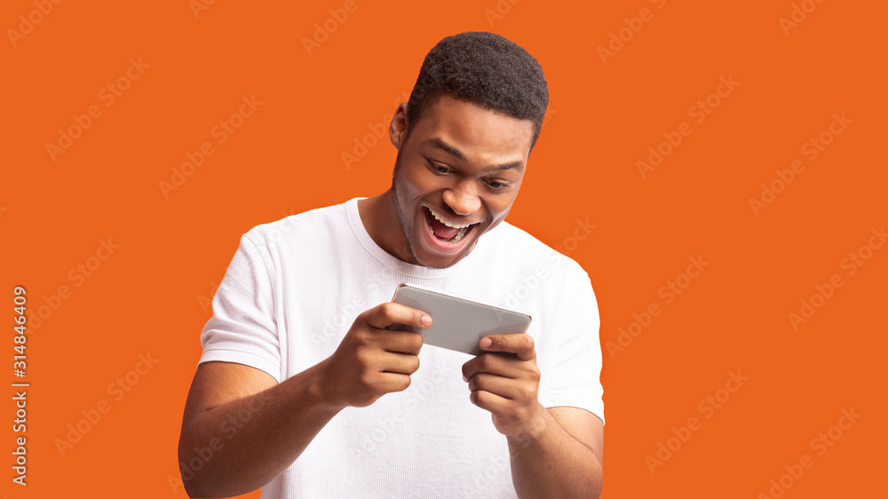 Excited afro man using mobile phone on orange background Excited afro man using mobile phone on orange background