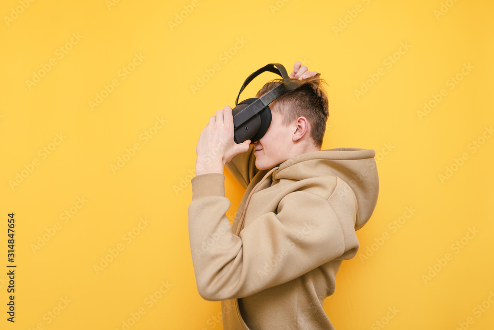 Guy in casual clothes wears a VR helmet and is about to play video games isolated on a yellow background. Young man testing a virtual reality helmet. VR gaming concept Guy in casual clothes wears a VR helmet and is about to play video games isolated on a yellow background. Young man testing a virtual reality helmet. VR gaming concept