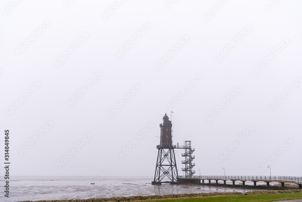 old lighthouse with low tide and fog at the northsea