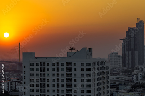 The background of the big sun that is hiding in the evening on the bridge over the river  is naturally beautiful and there are many tall buildings in the area below.