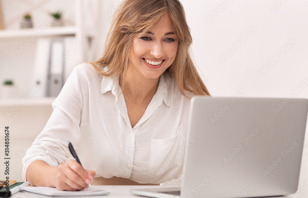 Businesswoman Taking Notes Working At Laptop Sitting At Workplace.