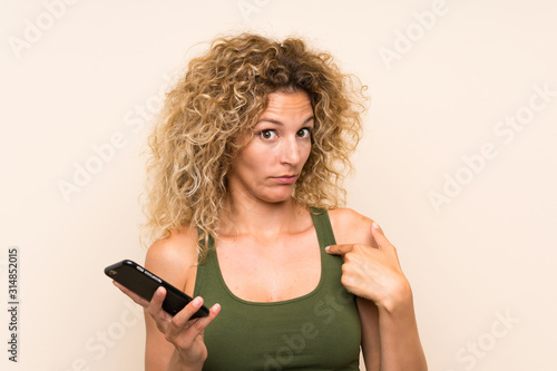 Young blonde woman with curly hair using mobile phone with surprise facial expression