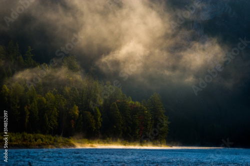 Early morning in siberian Sayan mountains. Fog above taiga forest on the mountain river bank. photo