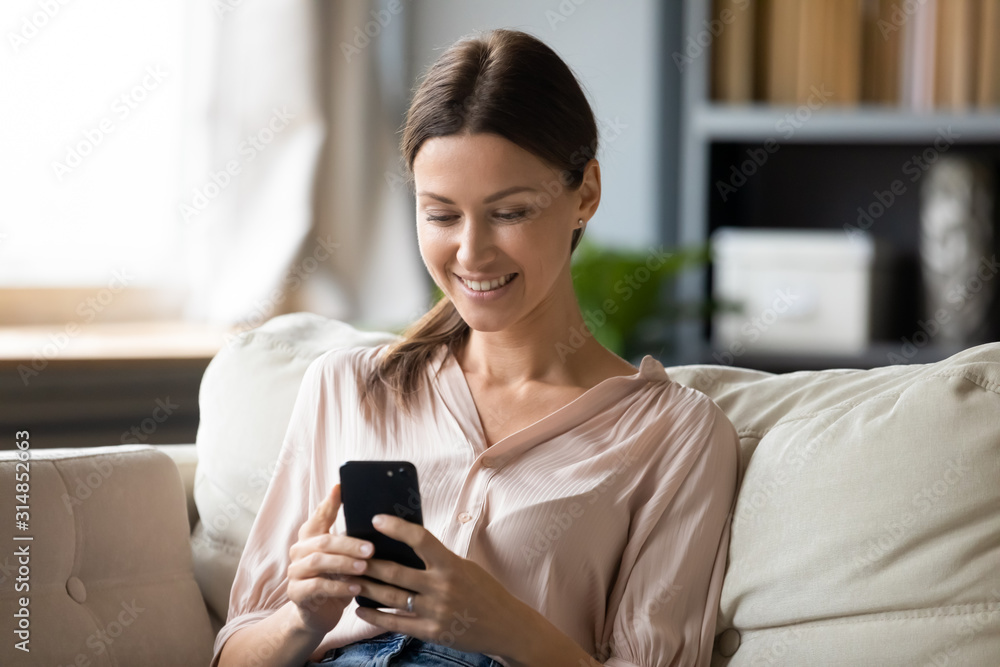 Smiling young woman using modern smartphone at home Smiling young woman using modern smartphone at home