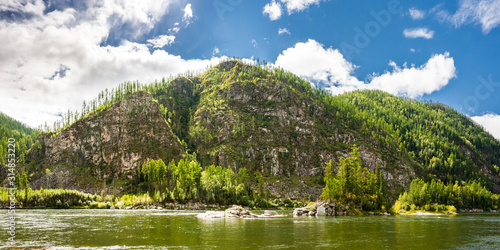 Steep rocky bank covered by taiga forest and the Small Yenisei river in sunny summer day. Siberia, Russia.