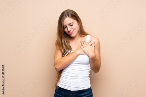 Teenager blonde girl over isolated background having a pain in the heart