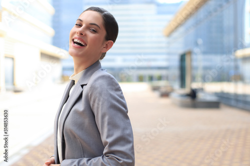 Attractive young woman in suit looking at camera and smiling while standing outdoors. © ty