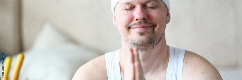 Fototapeta premium Sportsman with Closed Eyes Smiling Face Portrait. Bearded Man Doing Yoga Meditation with Hands Together. Peaceful Indoor Sport. Gymnastics Handsome Male Doing Relax Exercise Closeup Photography.