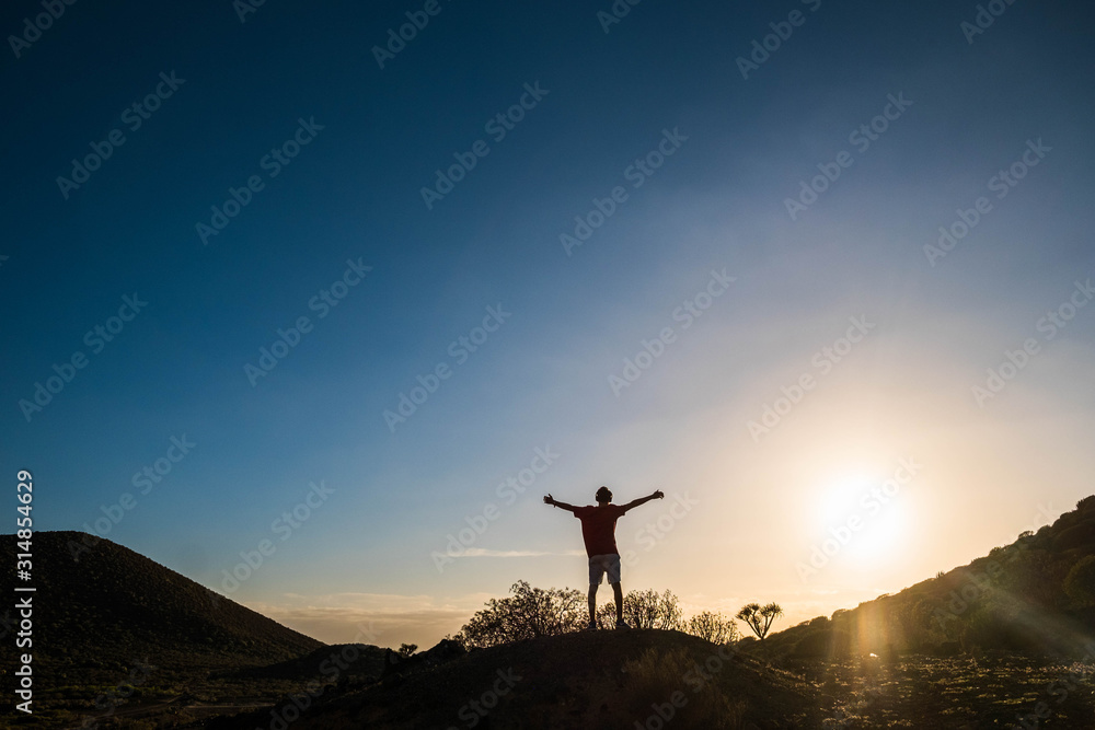 one isolated and alone man with opened arms on a hill looking at the sunset - active and healthy winner lifestyle concept - looking at the horizon