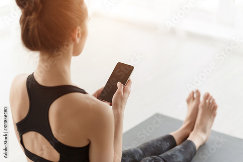 Girl using phone after practicing yoga on mat