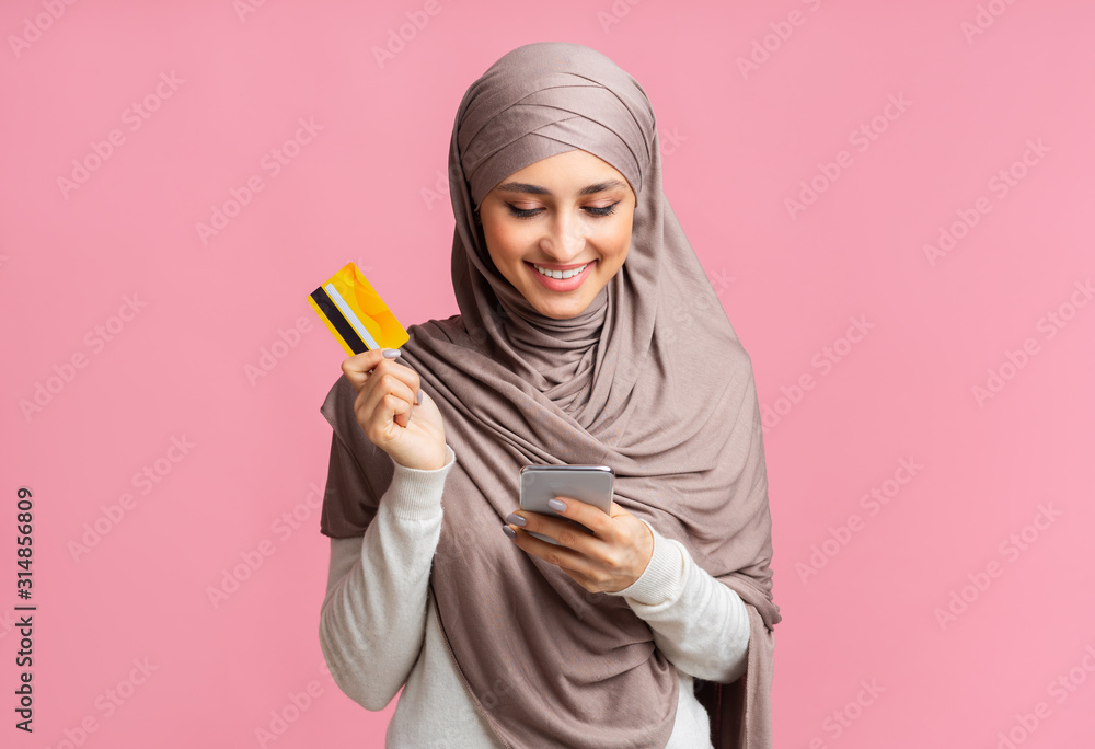 Happy muslim woman in headscarf using smartphone and holding credit card Happy muslim woman in headscarf using smartphone and holding credit card