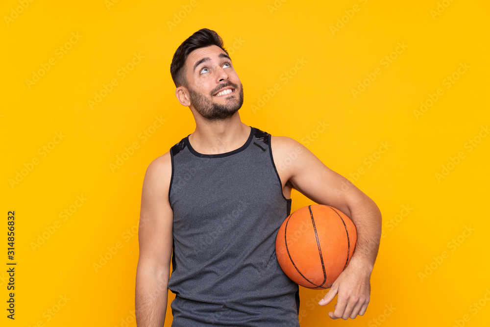 Handsome young basketball player man over isolated white wall looking up while smiling