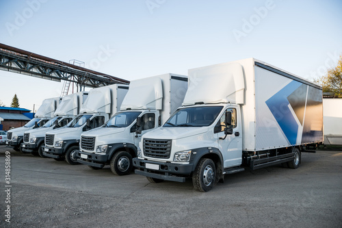 Five white truckers in the parking lot are waiting for the next delivery of goods. The concept of a transport company for the delivery of goods worldwide.