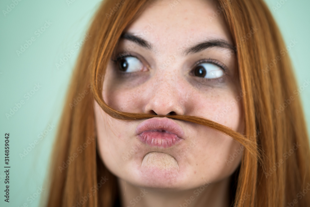 Close up portrait of funny girl holding long red hair like a mustache under her nose. Close up portrait of funny girl holding long red hair like a mustache under her nose.