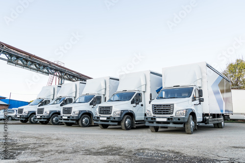 Five white truckers in the parking lot are waiting for the next delivery of goods. The concept of a transport company for the delivery of goods worldwide.