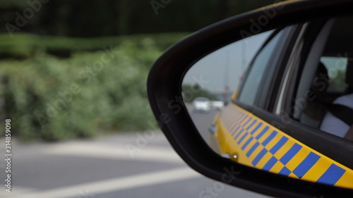 automobiles traffic on bridge against blurry seascape view in left side mirror of taxi vehicle extreme closeup