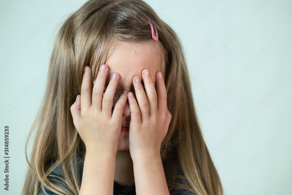 Close-up portrait of unhappy little girl with long hair covering her face with hands crying. Close-up portrait of unhappy little girl with long hair covering her face with hands crying.