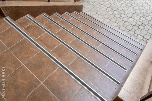 Concrete entrance stairs covered with ceramic tiles with metal railings outdoors.