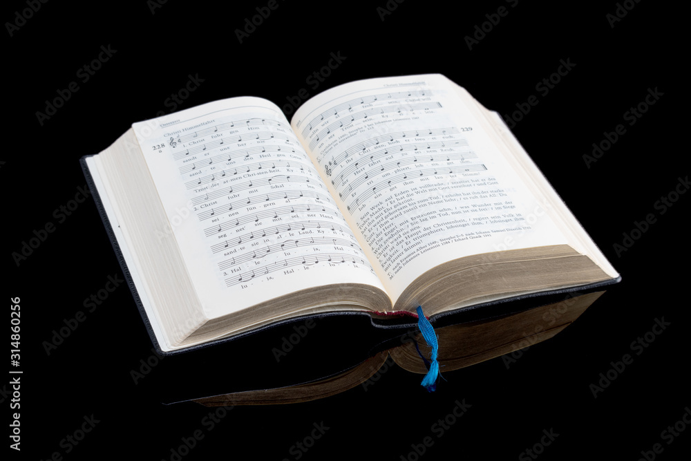 Aufgeschlagenes katholisches Gesangbuch mit Spiegelung isoliert auf schwarzem Hintergrund und Platz für Text Aufgeschlagenes katholisches Gesangbuch mit Spiegelung isoliert auf schwarzem Hintergrund und Platz für Text
