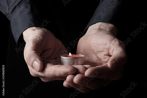 A man in a black shirt holds a candle in his hands, a symbol of loss