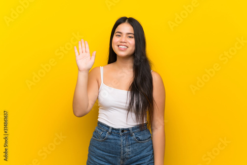 Young teenager Asian girl over isolated yellow background saluting with hand with happy expression