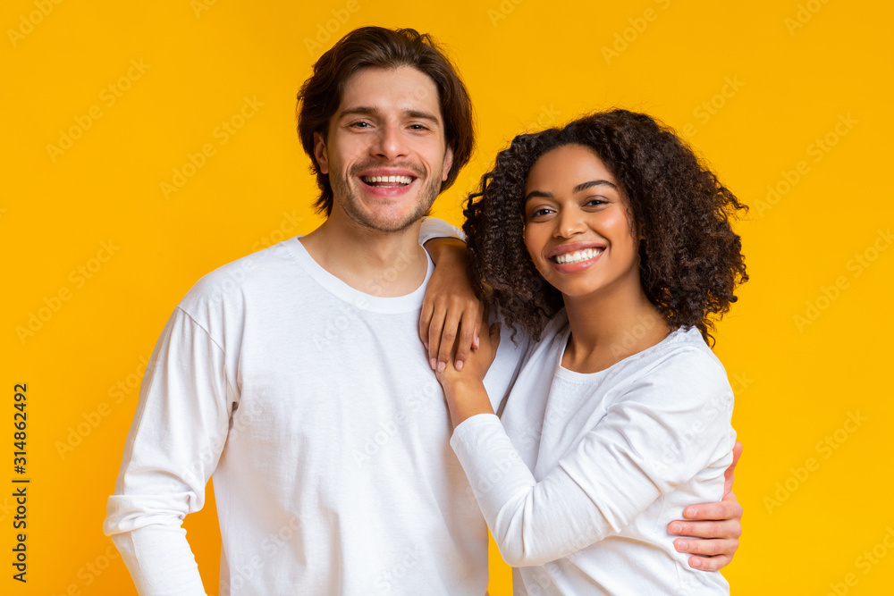 Romantic multiracial couple embracing, posing together and smiling at camera Romantic multiracial couple embracing, posing together and smiling at camera
