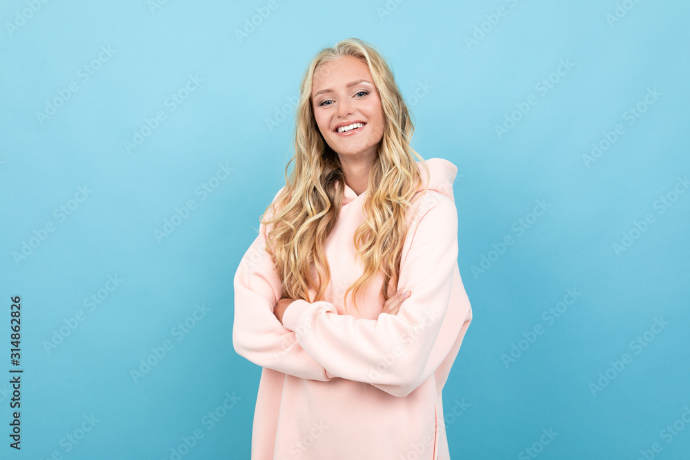 Caucasian woman with blonde hair in pink hoody smiles isolated on blue background Caucasian woman with blonde hair in pink hoody smiles isolated on blue background