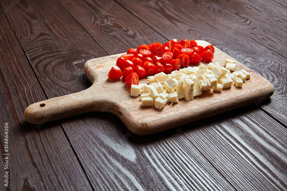 Fresh red cherry tomatoes with salad cheese on cutting board on brown wooden table Fresh red cherry tomatoes with salad cheese on cutting board on brown wooden table