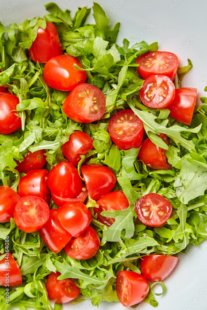 Red halved cherry tomatoes with fresh green arugula (rucola) leaves, closeup. Vegetable salad, top view Red halved cherry tomatoes with fresh green arugula (rucola) leaves, closeup. Vegetable salad, top view