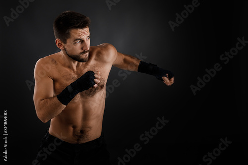 Sportsman boxer throwing a fierce and powerful punch. muscular man on black background.