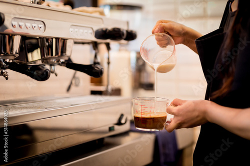 Woman barista pours milk into coffee making iced coffee.