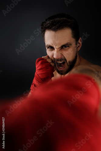 Sportsman boxer throwing a fierce and powerful punch forward in the camera. muscular man on black background.