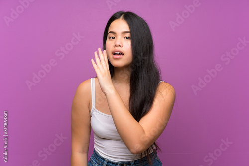Young teenager Asian girl over isolated purple background whispering something