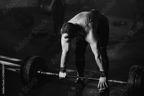 Black and white photo of an athlete exercising with barbell in a gym.
