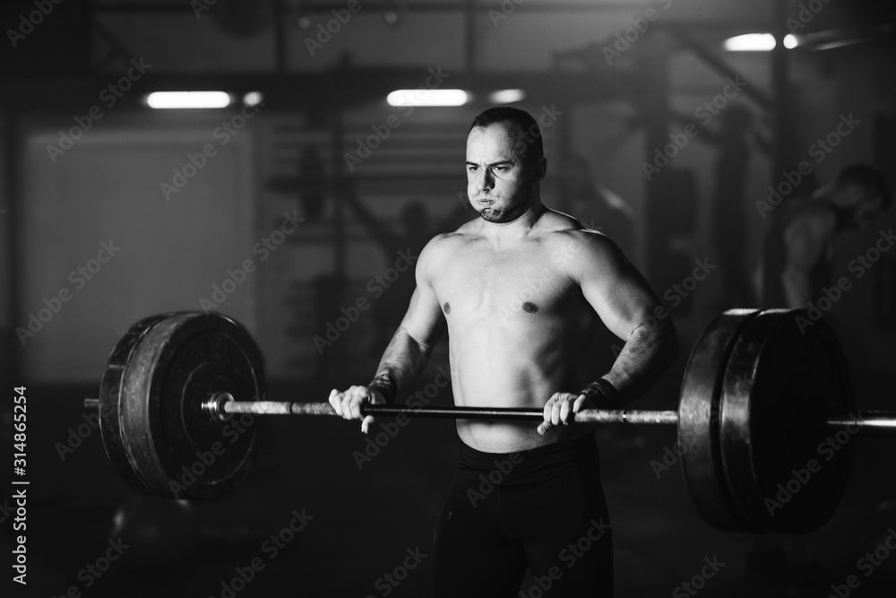 Fototapeta premium Muscular build man making an effort while exercising with barbell in a gym.