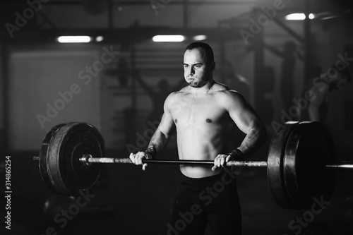 Muscular build man making an effort while exercising with barbell in a gym.