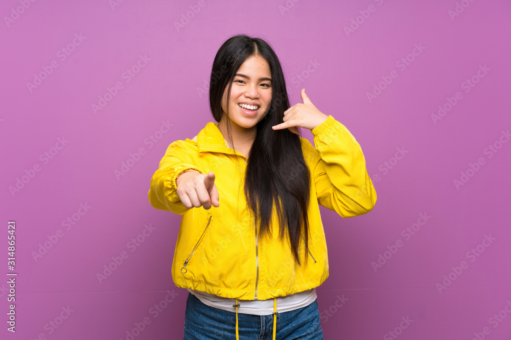 Young teenager Asian girl over isolated purple background making phone gesture and pointing front Young teenager Asian girl over isolated purple background making phone gesture and pointing front
