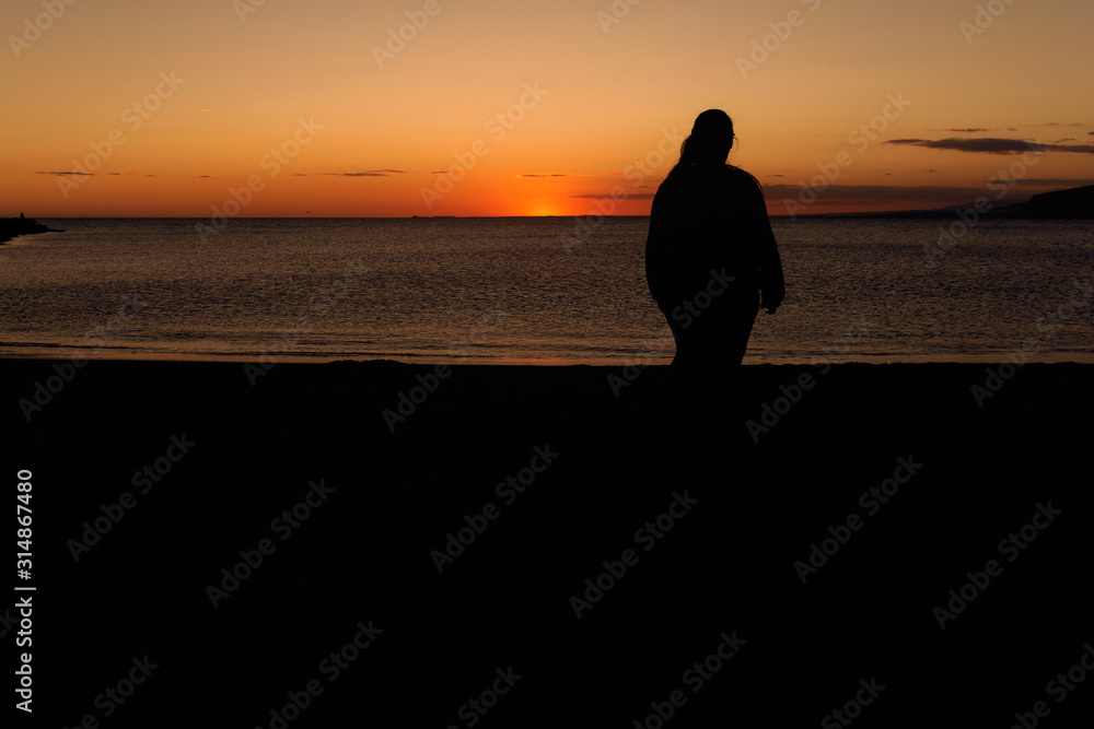 Silhouette of a young woman alone watching the sea during the sunset