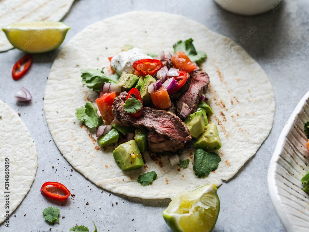 Tortillas with vegetables and beef steak slices. Avocados, tomatoes, red onions and meet with cilantro and lime juice in tortillas. Mexican food.