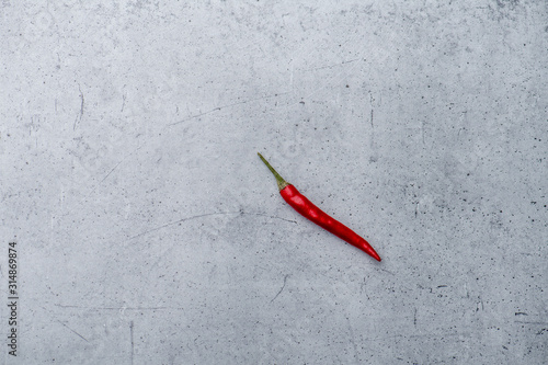Long shot of a single red chili pepper on a stone surface background.