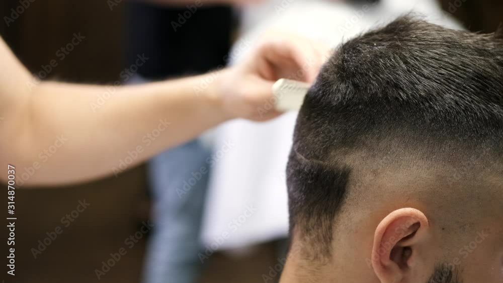 A barber is doing a hairstyle for the client. The customer has dark hair. The men are in the salon. A barber is doing a hairstyle for the client. The customer has dark hair. The men are in the salon.